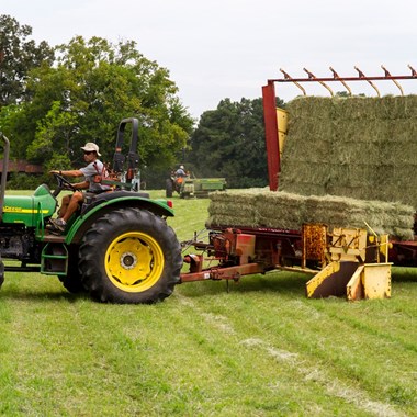Man driving tractor with machinery loading hay